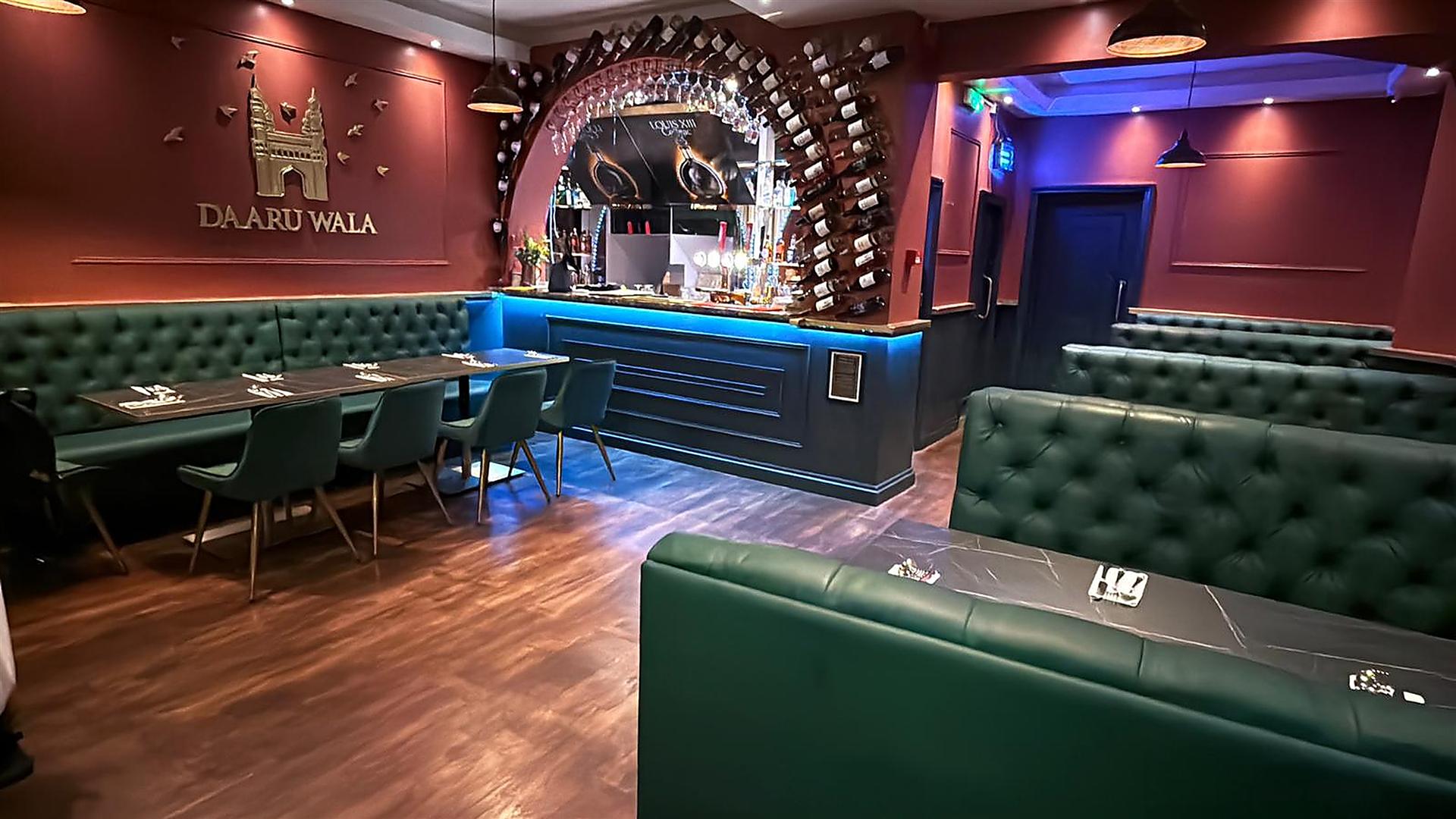 Warm and inviting dining area of Charminar Daaru Wala with cozy green leather booths